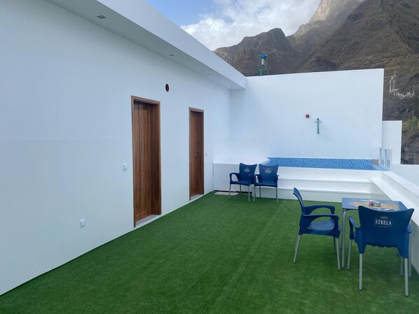 Un espacio exterior moderno con césped artificial, dos puertas de madera y una disposición de asientos con sillas azules.