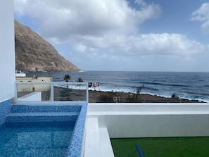 Una piscina en la azotea con vista al océano y una ladera rocosa.
