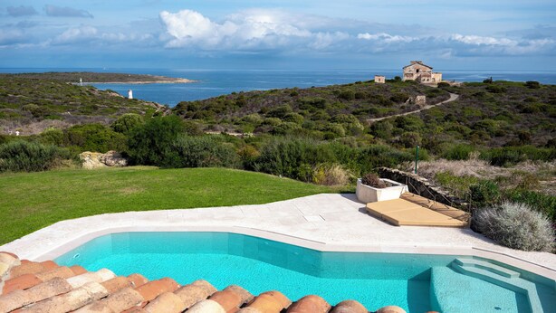 Una piscina con vistas al mar y una casa en una colina.