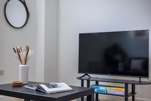 A living room with a flat-screen TV, a white vase with dried plants, a magazine, and a coffee table.