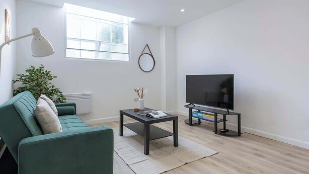 A modern living room with a sofa, a coffee table, a TV on a stand, a floor lamp, and a large window.