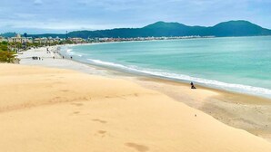 Una playa con arena, cielo despejado y una montaña al fondo.
