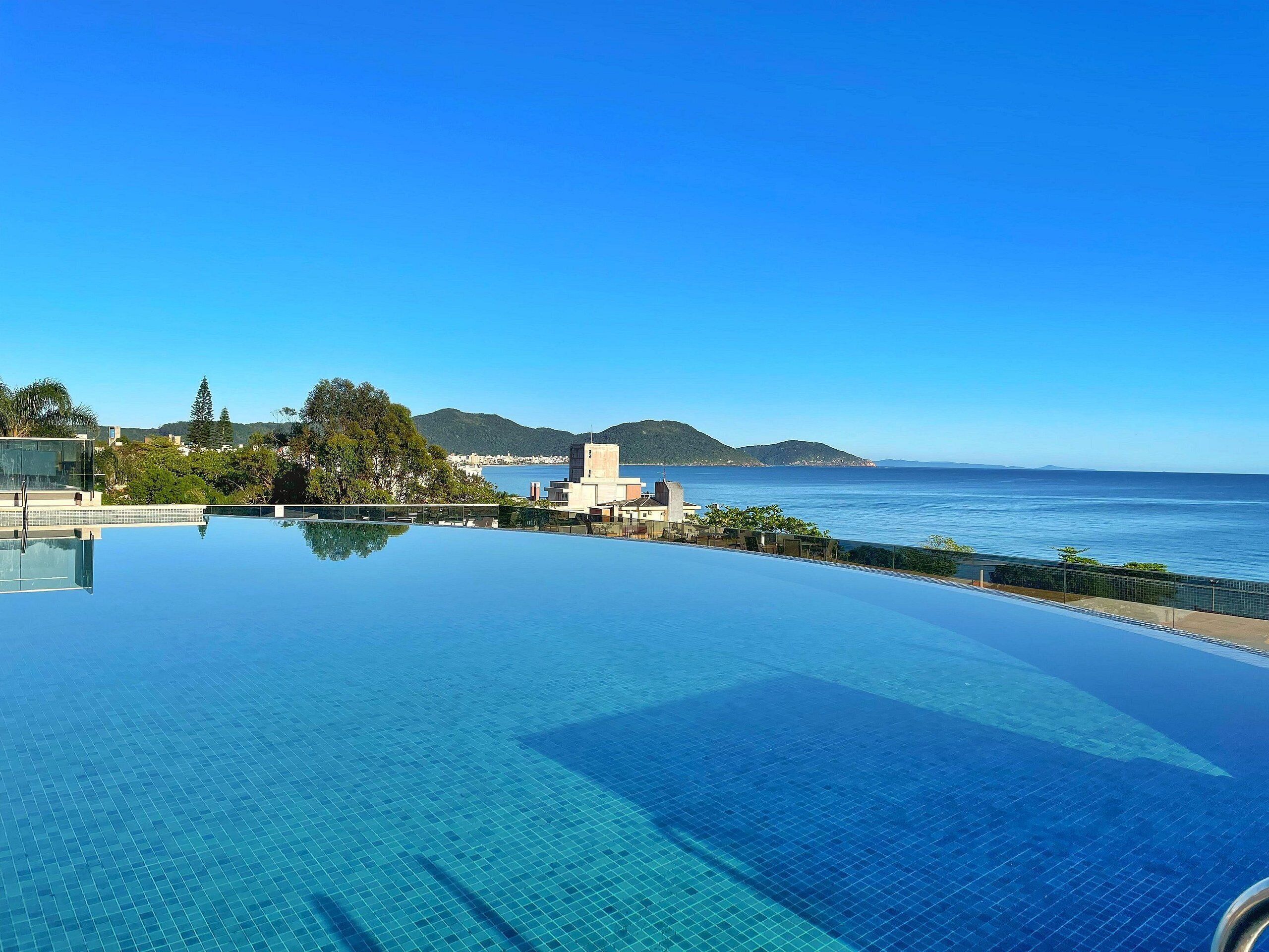A clear blue infinity pool with a view of the sea and distant hills.