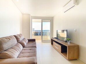 Una sala moderna con un sofá, un televisor sobre un mueble de madera y un balcón con vistas.
