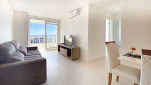 Una sala de estar moderna con un sofá, un televisor sobre un mueble de madera y una zona de comedor con una silla y mesa.