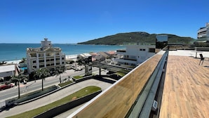 Ein modernes Gebäude mit einer Holzterrasse mit Blick auf eine Küstenlandschaft, inklusive Meerblick und einer entfernten Hügelkette.
