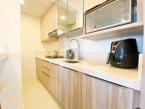 A modern kitchen with light wood cabinets, a stainless steel sink, a gas stove, a microwave, and an air fryer. - Espelho das Águas Residencial (Florianópolis)