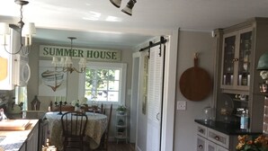 Une cuisine avec un plancher en bois, une table à manger et une pancarte sur laquelle on peut lire « MAISON D’ÉTÉ ».