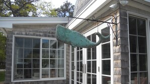 Une maison dotée d’une grande baie vitrée, d’un luminaire suspendu et d’un jardinier en bois orné de fleurs.