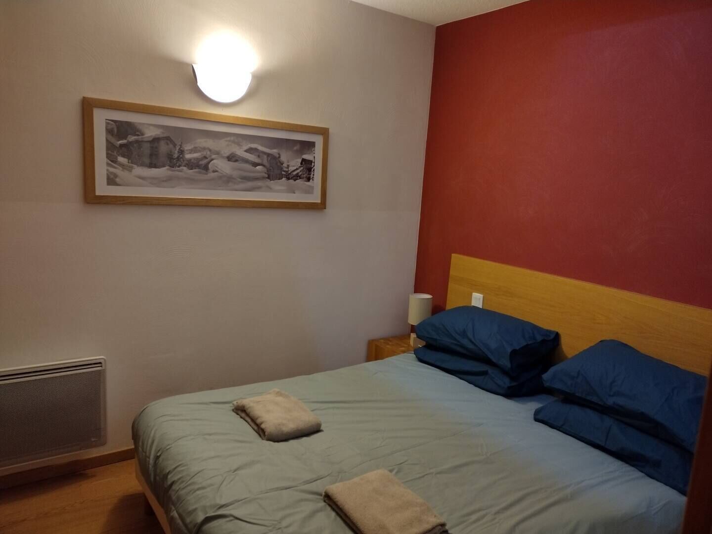 Un dormitorio con cama, mesita de noche, lámpara de pared y un cuadro enmarcado.