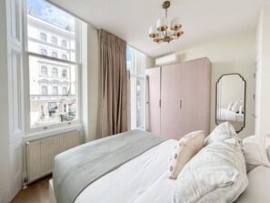 Enjoy a restful stay in this stylish bedroom with a large window offering a view of a historic building, a comfortable bed, and a modern chandelier.