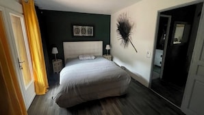 Ein Schlafzimmer mit einem großen Bett, einem Nachttisch mit Lampe, einem Wanddekor und einer Tür zu einem anderen Raum.