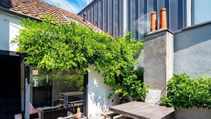 A patio area with a pergola covered in greenery, a concrete planter with plants, and a wooden table and chairs. - Verne Dreams (Ghent)