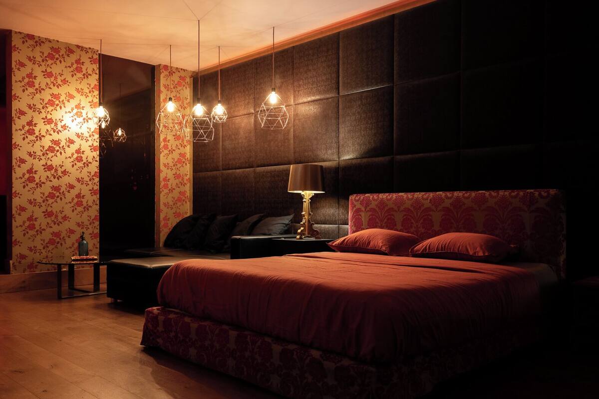 A bedroom with a large bed, a nightstand, a lamp, and a wall with floral wallpaper.