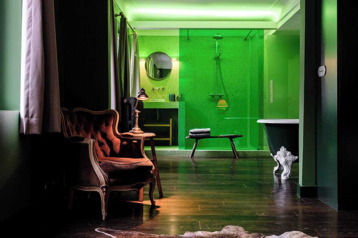 A modern interior with a green wall, a wooden chair, a small table, and a bathtub.
