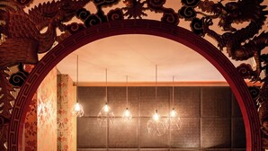 A room with a dark-colored sofa set, a small table with a lamp, and a decorative archway with intricate designs. - Verne Dreams (Ghent)