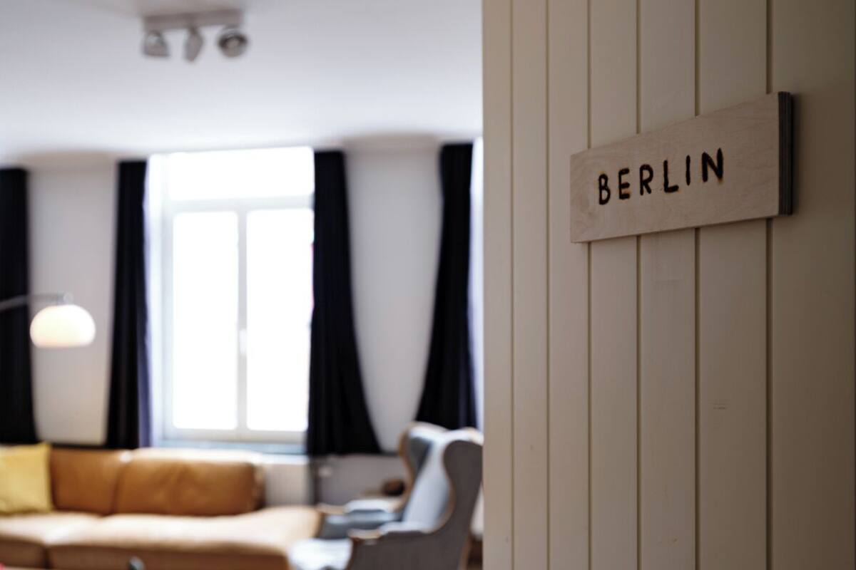 A modern living room with a wooden door labeled "BERLIN," a sofa, a chair, and a lamp.