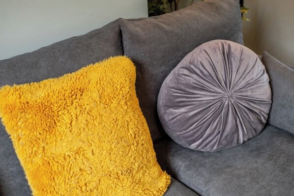 A grey sofa with a fluffy yellow throw pillow and a circular grey pillow. - Comfortable 3 Bedroom Townhouse (Northampton)