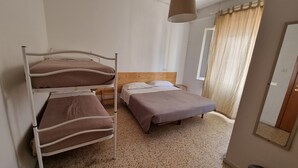 Una habitación con literas, una cama individual, un cabecero de madera, una mesita de noche pequeña y una ventana con cortinas.