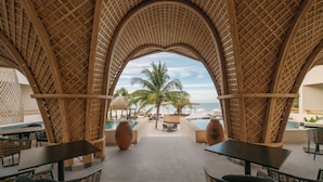An indoor area with a view of the beach, featuring a thatched roof, tables, chairs, and a pool. - Ana y Jose Holbox Boutique All Inclusive Hotel (Isla Holbox)
