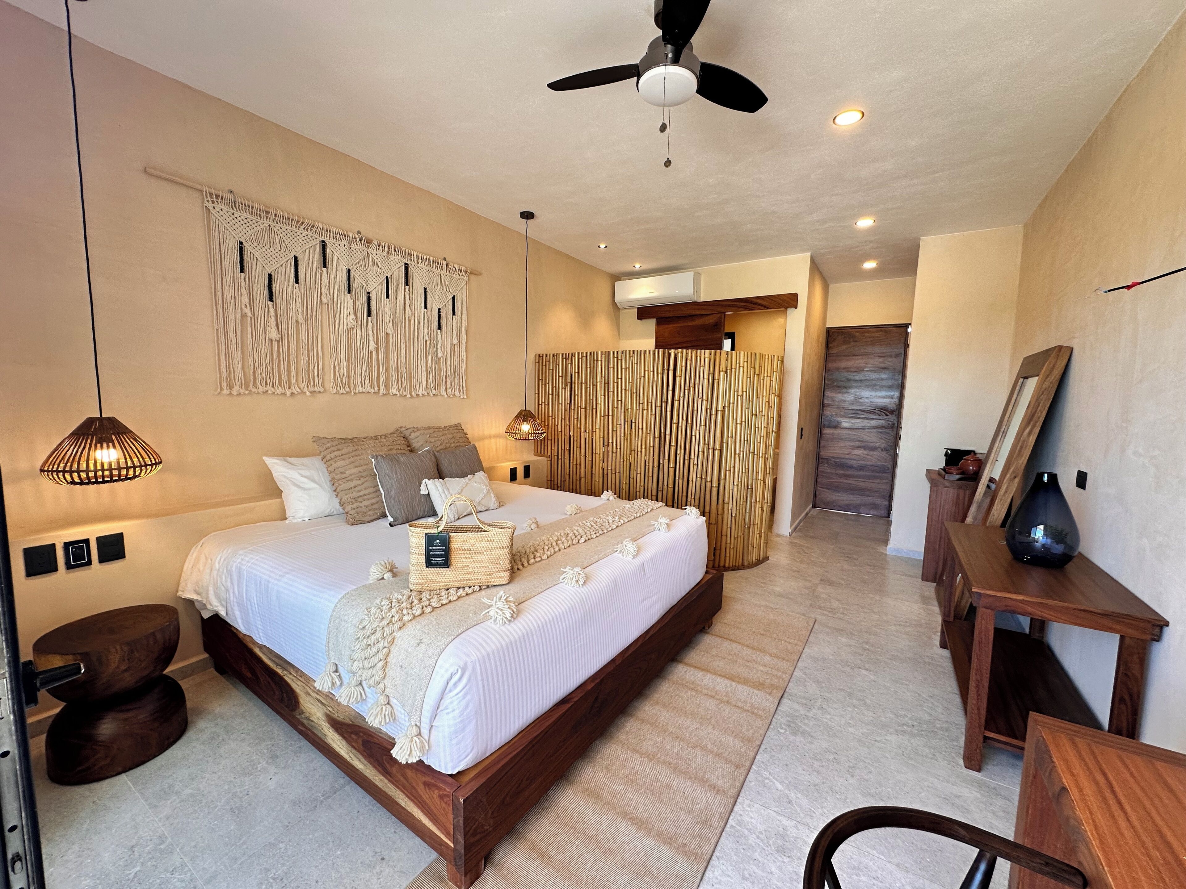 Un dormitorio moderno con una cama de madera, decoración de macramé en la pared, un ventilador de techo y una mesita de noche con un florero.