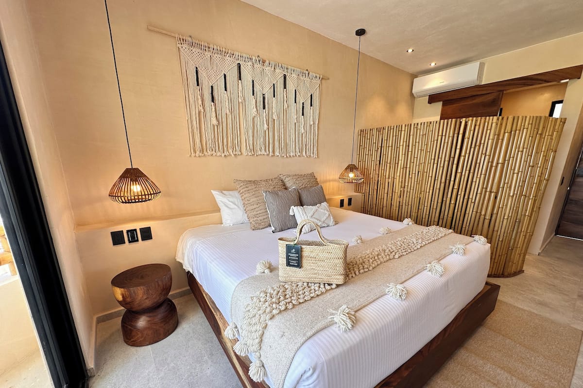 Une chambre spacieuse avec un grand lit, des décorations murales en macramé et une cloison en bambou.