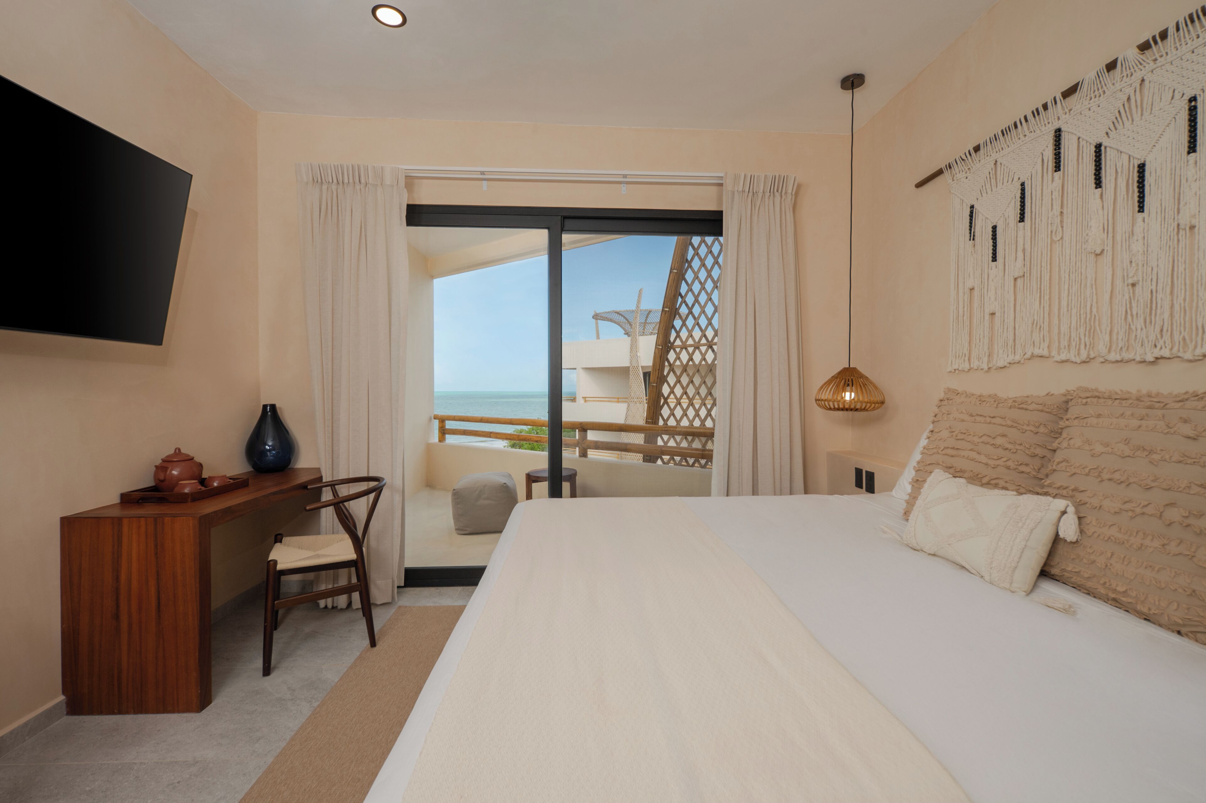 Ein Hotelzimmer mit Bett, Schreibtisch, Fernseher, Meerblick und einem Balkon.