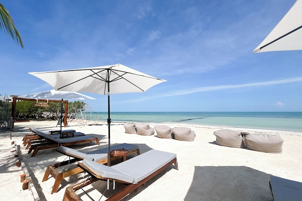 En la playa, arena blanca, sillas reclinables de playa, sombrillas