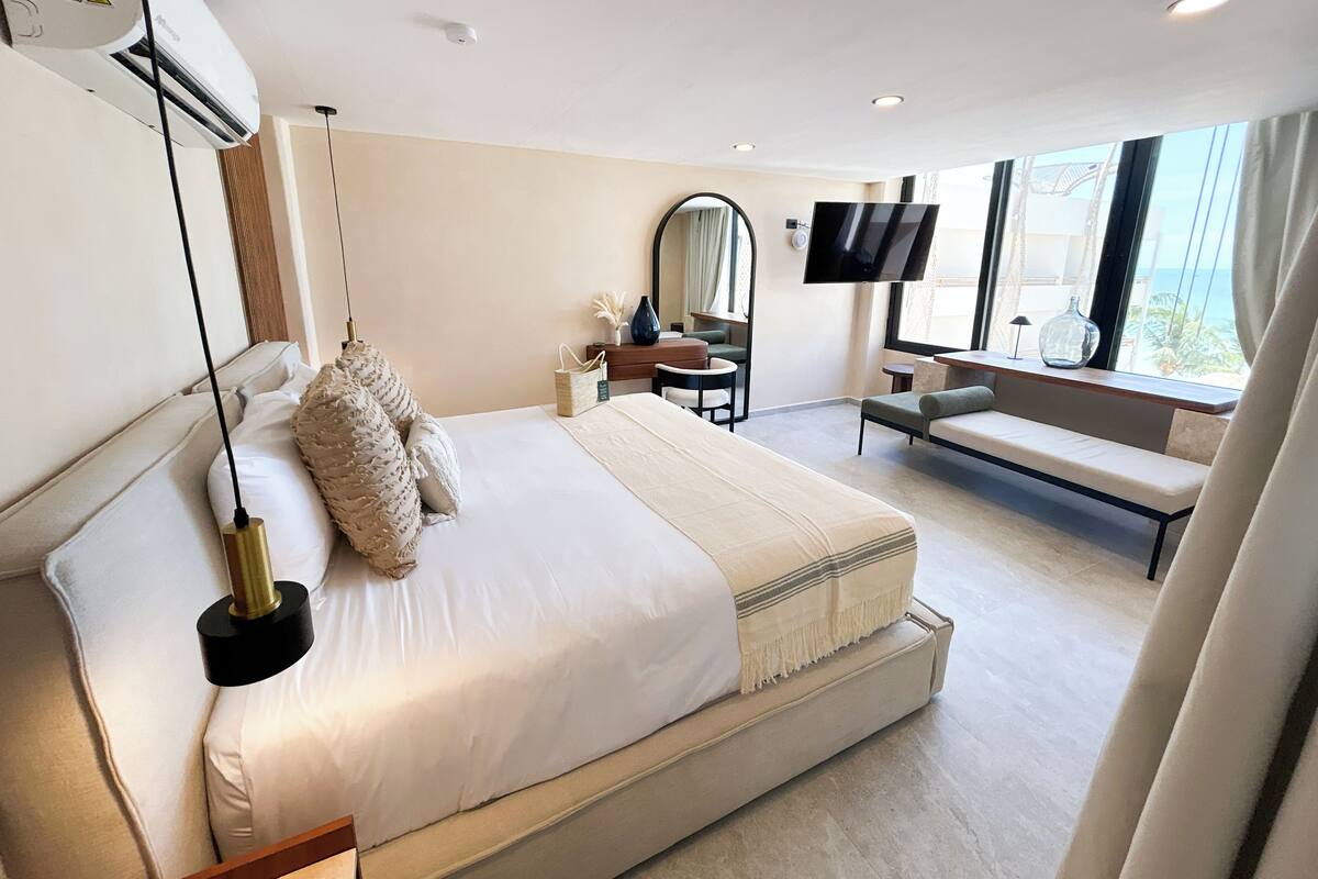 Une chambre d’hôtel moderne dotée d’un grand lit, d’un bureau, d’une télévision et offrant une vue sur l’océan.