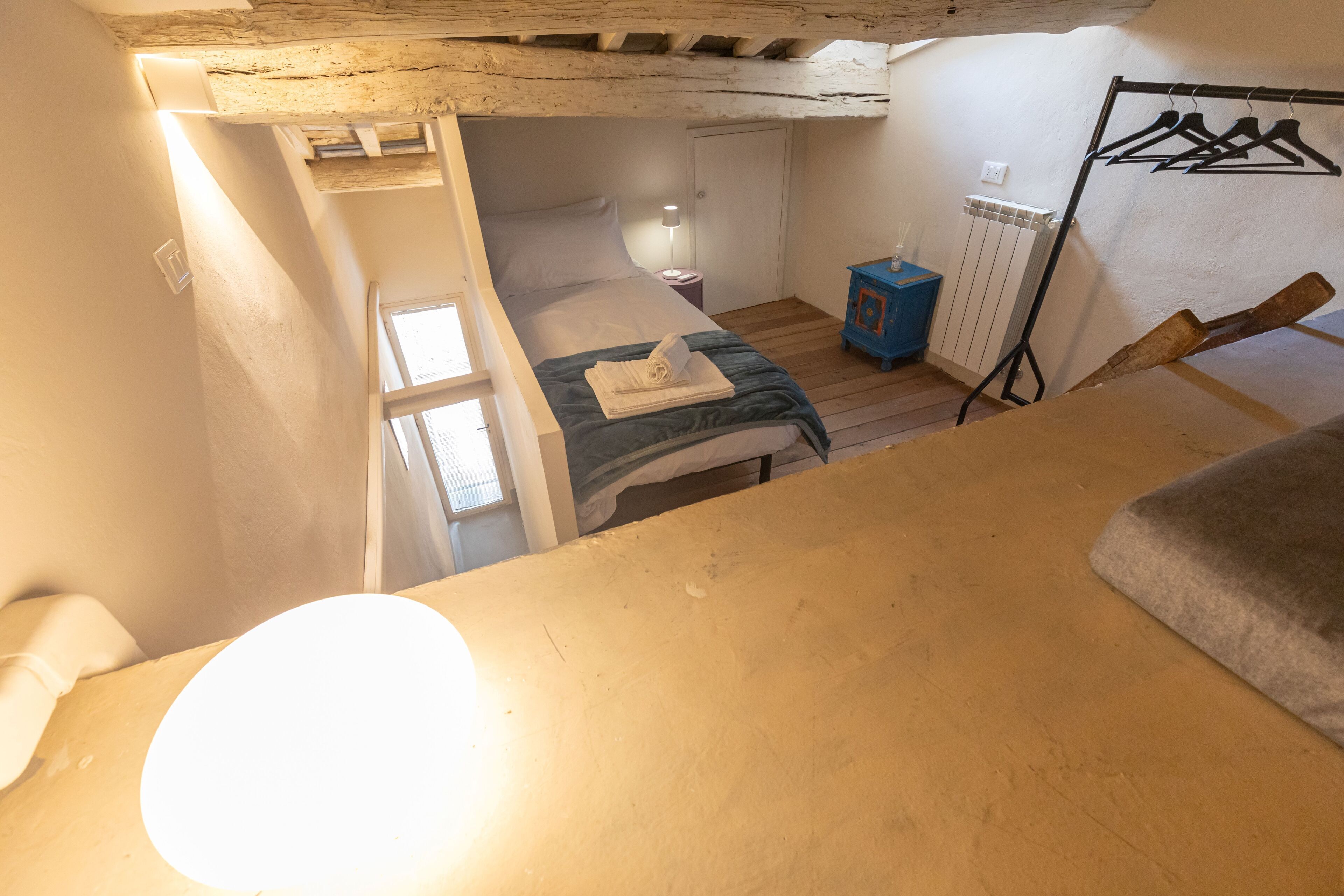 A compact bedroom with a single bed, a bedside table, a radiator, and a clothing rack.