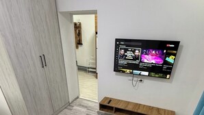 Een kamer met een houten garderobe, een wandgemonteerde televisie, een houten salontafel en een kamerkleed met dessin.