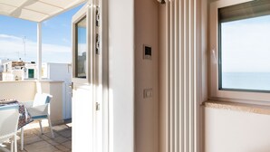 Ein Balkon mit Tisch und Stühlen, Blick auf das Meer, und ein Fenster mit Meerblick.