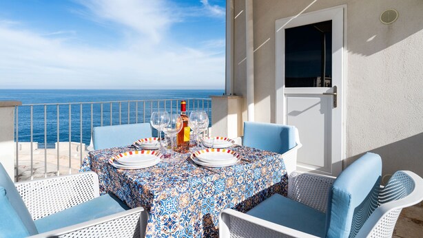 Ein Tisch auf dem Balkon mit Tellern, Gläsern und einer Flasche, mit Blick aufs Meer.