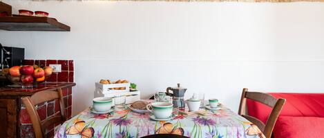 Un comedor con una mesa preparada para dos personas, con mantel floral, sillas de madera y un sofá rojo.