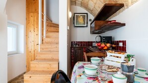 Eine Holztreppe führt zu einer Küche mit gefliestem Rückspritzschutz, einem Esstisch, der mit Schüsseln, Tellern und einer Kaffeemaschine gedeckt ist.