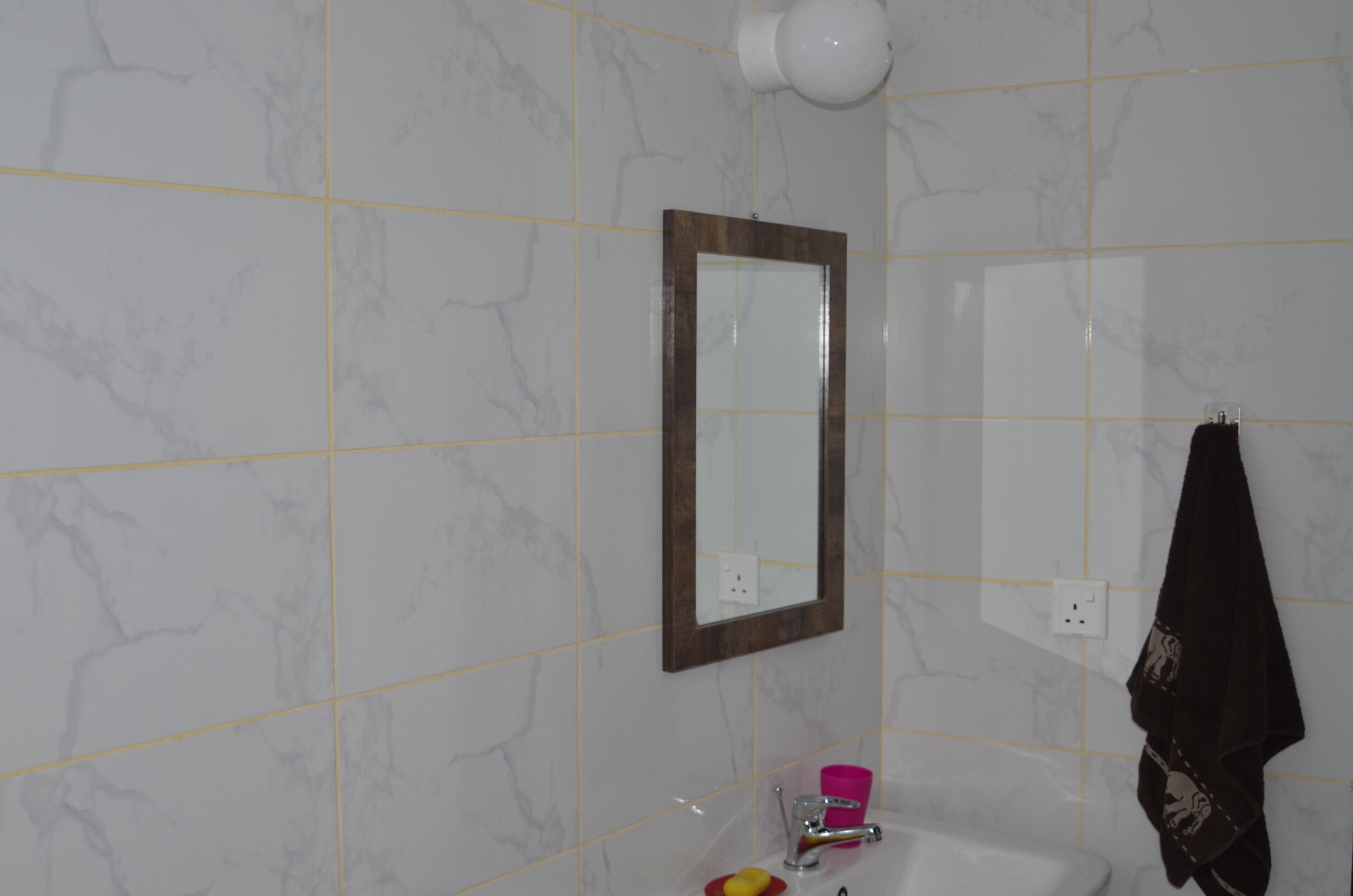 A bathroom with a marble wall, a mirror, a sink, and a towel hanging on the wall.