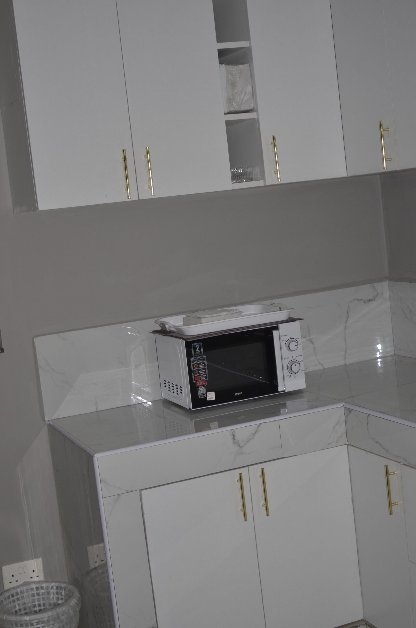 Une cuisine avec des meubles blancs, un four à micro-ondes et un plan de travail en marbre.