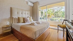 A hotel room with a large bed, a wooden nightstand, a chair, and a view of the outdoors. - Lux Garden View by Madeira Sun Travel (Funchal)