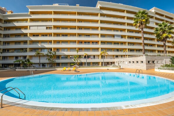 A large swimming pool with a multi-story hotel building in the background.