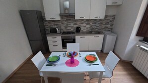 Une petite cuisine avec des meubles blancs, un four à micro-ondes, une cuisinière et un évier. On y trouve une table avec des chaises et de l’argenterie disposée pour un repas.