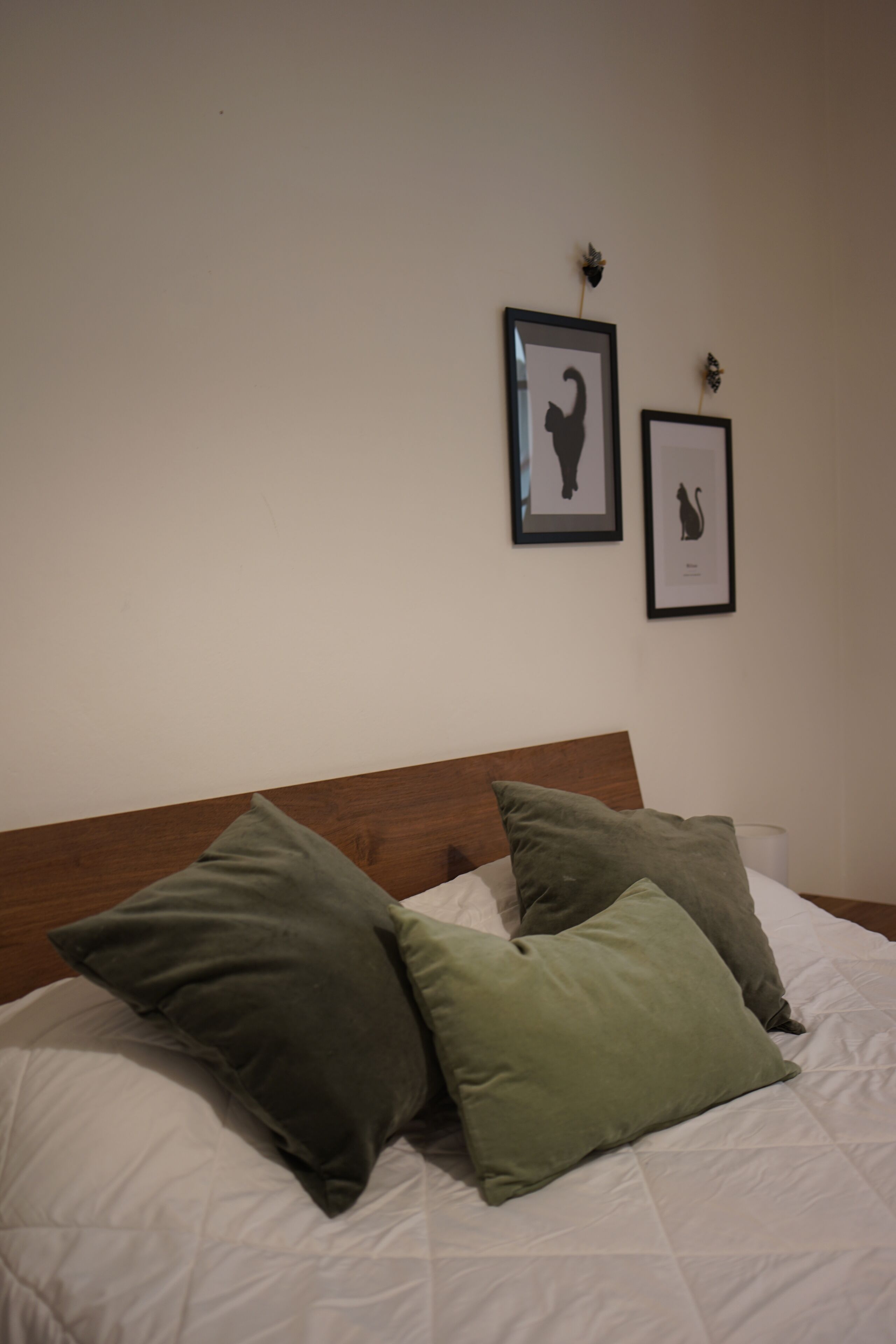 A neatly made bed with green pillows and two framed pictures on the wall above.