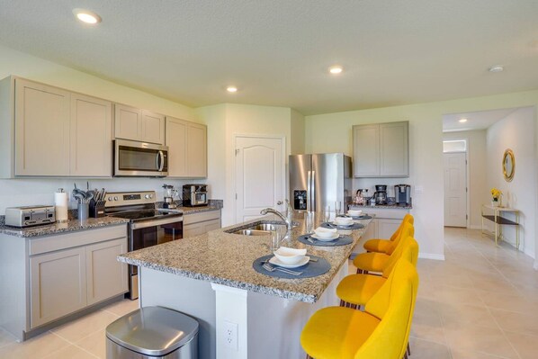 A modern kitchen with granite countertops, stainless steel appliances, and yellow bar stools. - Charming Haines City (Haines City)