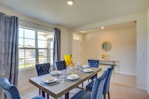 A dining area with a long table set for six, blue upholstered chairs, a vase with yellow flowers, and a round mirror on the wall. - Charming Haines City (Haines City)