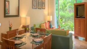A dining area with a table set for two, a green sofa, and a television in the corner. - Mayan Palace Vidanta Resort Riviera Maya 1 BR studio (Cancun)