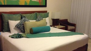 A neatly made bed with a green blanket, multiple pillows, a wooden headboard, a nightstand with a lamp, and a chair. - Mayan Palace Vidanta Resort Riviera Maya 1 BR studio (Cancun)