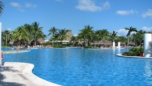 A large, clear swimming pool with palm trees and thatched-roof structures in the background. - Mayan Palace Vidanta Resort Riviera Maya 1 BR studio (Cancun)