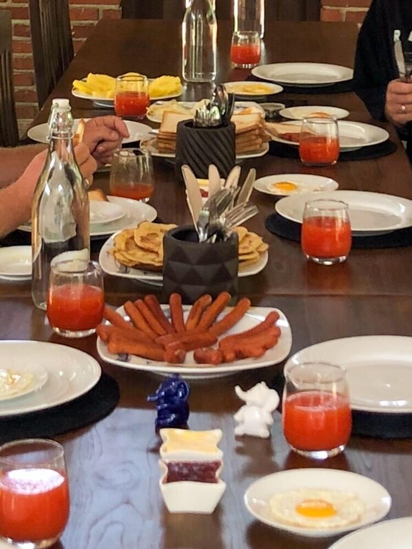 Una mesa con platos de comida, que incluyen salchichas, huevos y tostadas. También hay salsas y una botella de jugo.