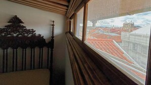 A room with a wooden headboard and a window with a view of buildings. - Casa Quixote (Braga)