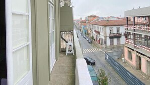A balcony with a view of a street lined with buildings, a white chair, and a small table. - Casa Quixote (Braga)