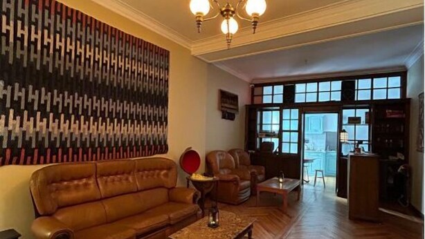 A spacious living room with a brown leather sofa, a patterned rug, and a wooden floor. - Casa Quixote (Braga)